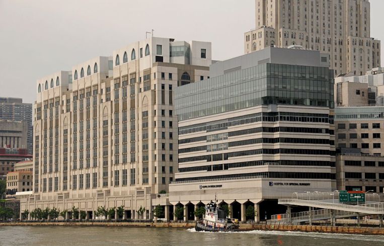A large grey building with a glass top on a river as a boat passes.