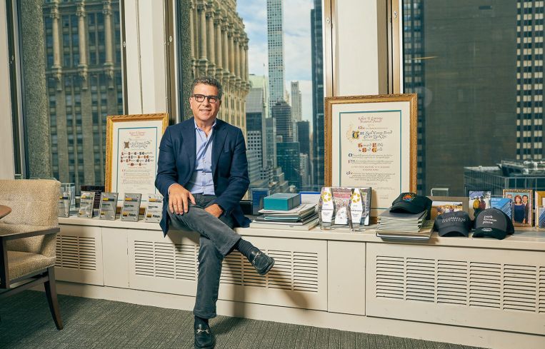 A man leaning against a shelf with a cityscape behind him through the window.