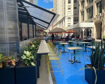 Several tables and chairs on blue pavement on a New York City street.