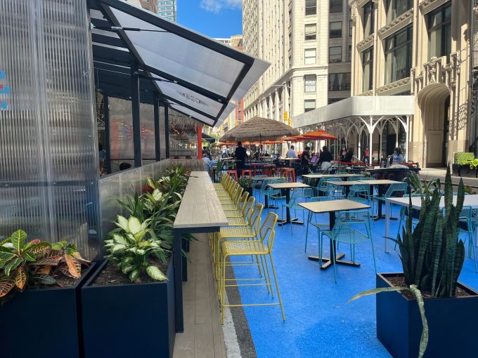 Several tables and chairs on blue pavement on a New York City street.