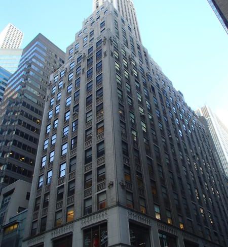A large grey skyscraper ascends multiple stories into a cloudless sky.