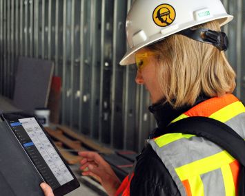 A woman in a hardhat on a construction site looking at a tablet.