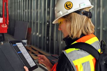 A woman in a hardhat on a construction site looking at a tablet.