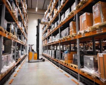 A man works with a forklift between warehouse shelves in a logistics terminal of a manufacturer of ... forklifts.