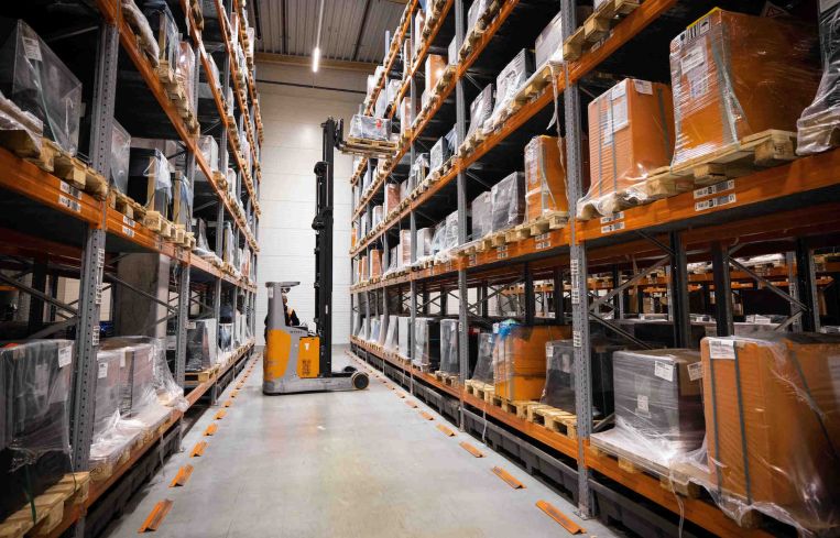 A man works with a forklift between warehouse shelves in a logistics terminal of a manufacturer of ... forklifts.