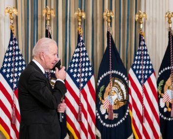 U.S. President Joe Biden removes a protective face mask before delivering remarks on the October jobs reports in the State Dining Room at the White House on Nov. 5, 2021 in Washington, DC. He is backed by American flags.