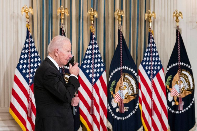 U.S. President Joe Biden removes a protective face mask before delivering remarks on the October jobs reports in the State Dining Room at the White House on Nov. 5, 2021 in Washington, DC. He is backed by American flags.