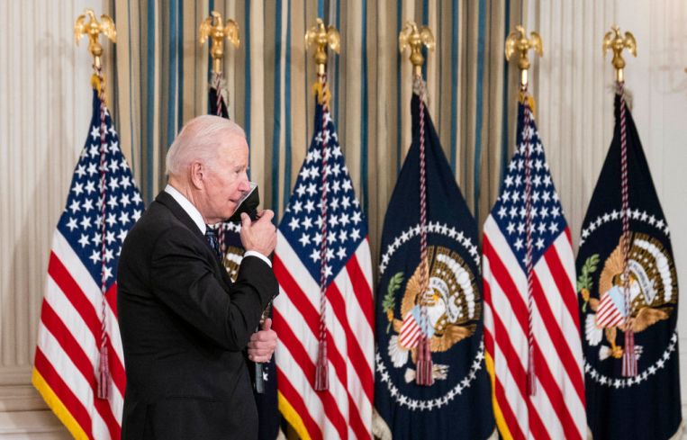 U.S. President Joe Biden removes a protective face mask before delivering remarks on the October jobs reports in the State Dining Room at the White House on Nov. 5, 2021 in Washington, DC. He is backed by American flags.