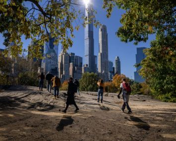 TOPSHOT - People stand beneath fall foliage and before high-rise buildings of the Manhattan city skyline in Central Park in New York on November 5, 2021. - merica's northeast is famous for its red, orange and yellow fall foliage but experts say climate change is dulling the colors and delaying peak season, causing concern for the region's multibillion-dollar "leaf-peeping" tourist industry. Warmer temperatures and heavier rainfall are keeping leaves greener for longer while extreme weather events like heatwaves and storms are stripping trees bare before getting to autumn, according to conservationists. (Photo by Ed JONES / AFP) (Photo by ED JONES/AFP via Getty Images)