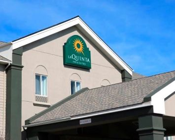 A La Quinta Inn and Suites motel rises into the frame with a peaked roof backed by a blue sky.