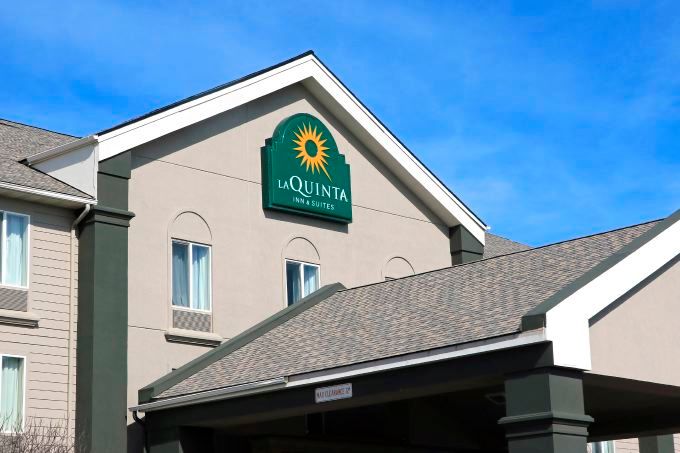 A La Quinta Inn and Suites motel rises into the frame with a peaked roof backed by a blue sky.