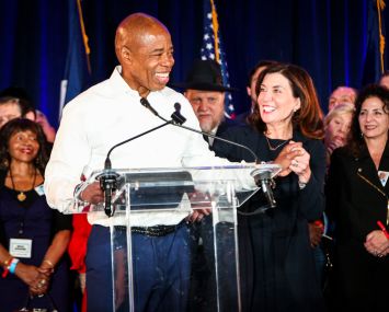 A man at a podium, smiling, surrounded by other people.