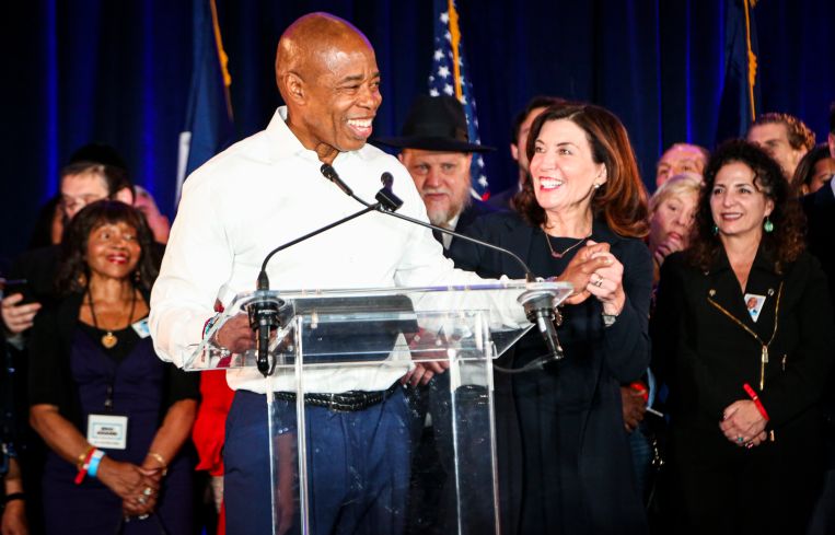 A man at a podium, smiling, surrounded by other people.