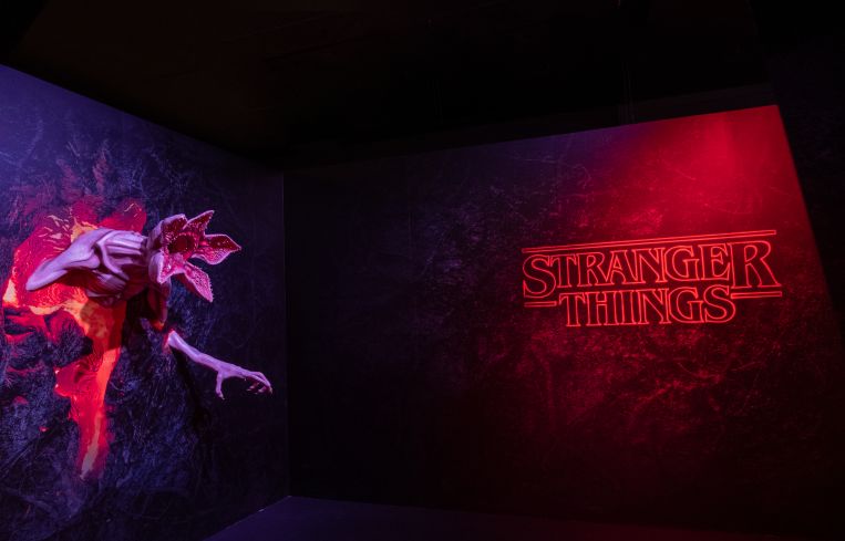 The words "Stranger Things" lighted in red with a monster protruding from the wall.