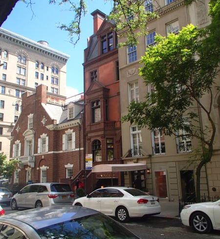 The red building at 26 East 64th Street, partially obscured by a low-hanging tree branch.