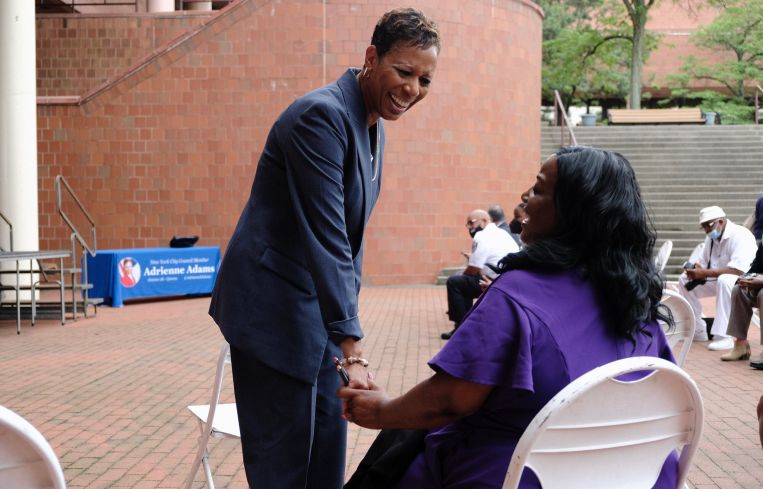 Queens Councilmember Adrienne Adams speaks with a seated woman outside a brick building.