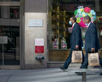 Two people wearing masks holding Shake Shack bags walk past a WeWork office building amid the coronavirus pandemic on May 12, 2020 in New York City.
