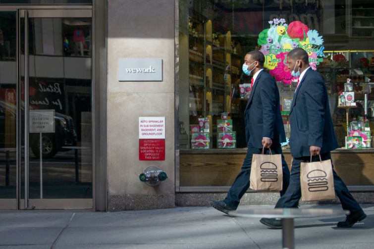 Two people wearing masks holding Shake Shack bags walk past a WeWork office building amid the coronavirus pandemic on May 12, 2020 in New York City.