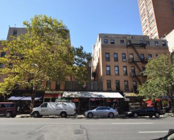 Two medium-sized apartment buildings with one partially obscured by a tree across a street in New York City's Upper East Side neighborhood.