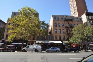 Two medium-sized apartment buildings with one partially obscured by a tree across a street in New York City's Upper East Side neighborhood.