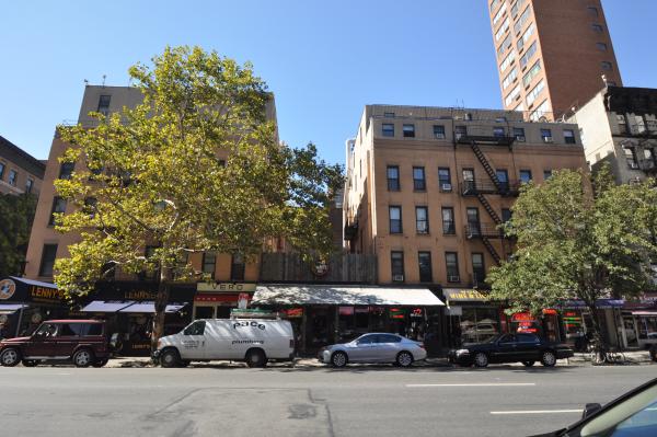 Two medium-sized apartment buildings with one partially obscured by a tree across a street in New York City's Upper East Side neighborhood.