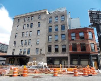 Two larger white buildings next to a shorter red building on the right fronted by orange traffic cones.