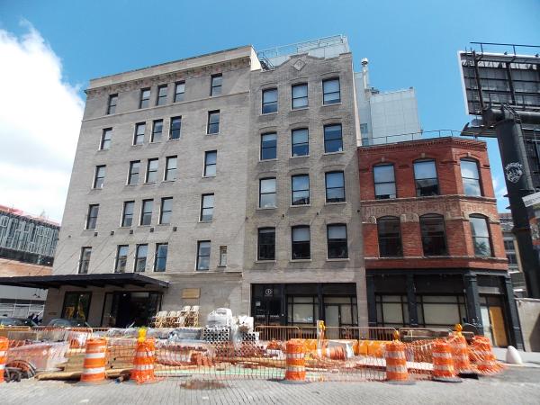 Two larger white buildings next to a shorter red building on the right fronted by orange traffic cones.