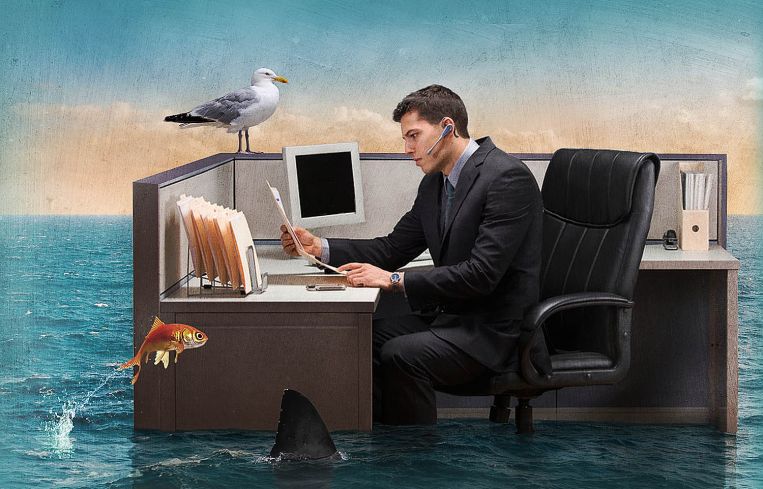 An illustration of a man at an office cubicle as the floor around him floods with water, sharks and fish.