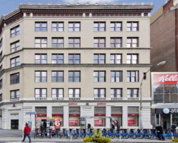 A photo of 860 Broadway, a large grey building in between two shorter ones.