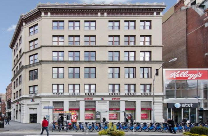 A photo of 860 Broadway, a large grey building in between two shorter ones.