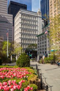 The tall concrete building in the Financial District at 195 Broadway, as seen with a garden of flowers in front of it.