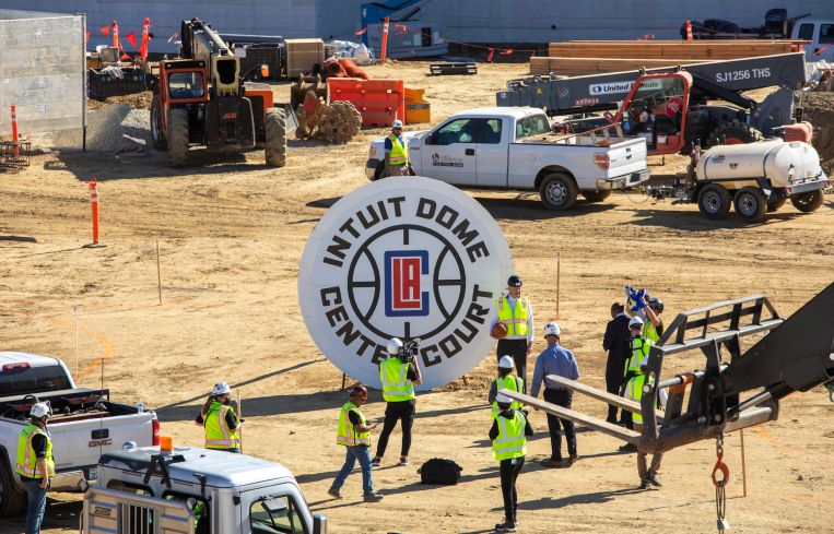 Jerry West, top, poses for photos holding a basketball at the site of the Intuit Dome, the new home of the Los Angeles Clippers, under construction this month in Inglewood, Calif.