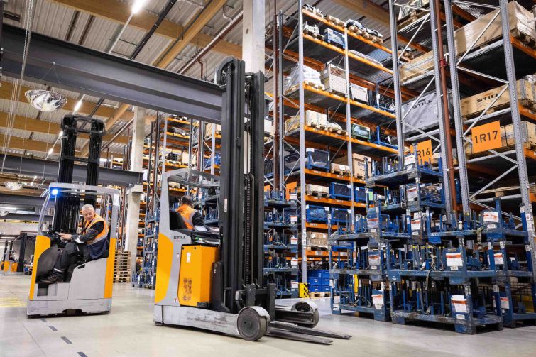 Two forklifts are between storage racks in a logistics terminal.