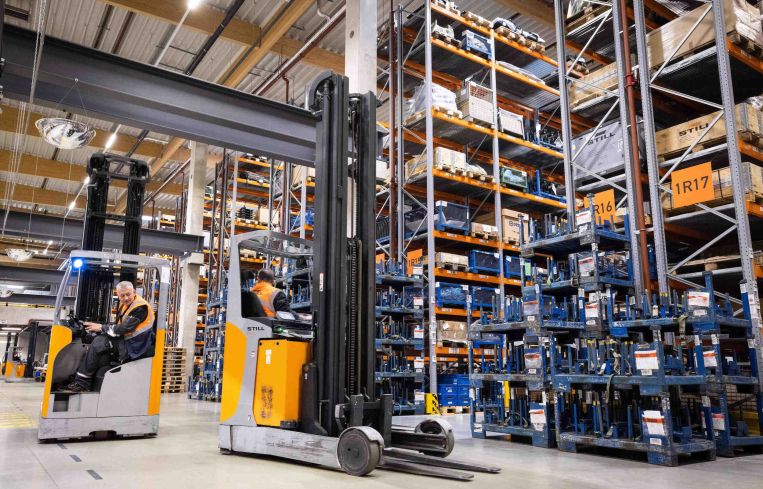 Two forklifts are between storage racks in a logistics terminal.