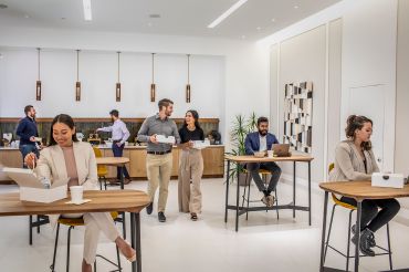 In a Convene location in New York City, workers mill about in a shared room with wooden desks and white walls.