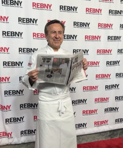 Chef Daniel Boulud holds a newspaper with an article about him on a red carpet at the 2022 REBNY Gala.