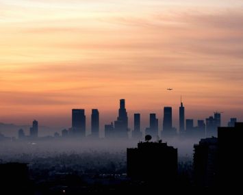 A plane flies over the Los Angeles, California, skyline at sunrise.