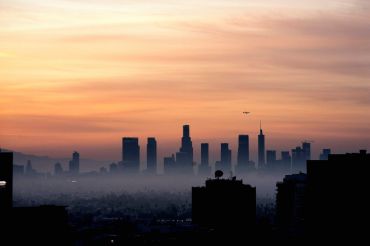 A plane flies over the Los Angeles, California, skyline at sunrise.