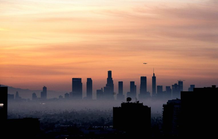 A plane flies over the Los Angeles, California, skyline at sunrise.