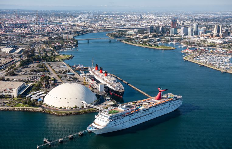 The Carnival Airship flies over the Queen Mary, top, and the cruise ship Carnival Imagination, bottom, in Long Beach.