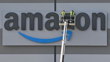 Craftsmen work on the Amazon logo at a shipping warehouse.
