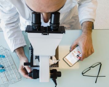 Mature scientist male in his 50s wearing a lab coat looking through a microscope in a laboratory. Basque Country, Spain, Europe.