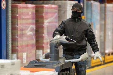 An employee with a warming face mask drives through a refrigerated warehouse.