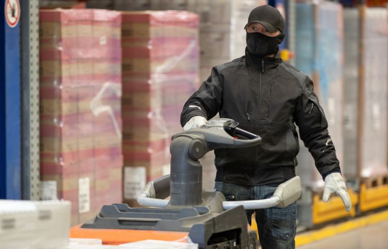 An employee with a warming face mask drives through a refrigerated warehouse.