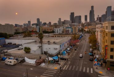 An aerial view of homeless encampments in Skid Row as smoke from California wildfires obscures the setting sun and skyline in 2021.