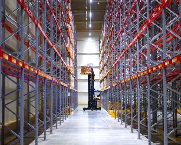 A forklift truck lifts goods into a storage rack in a warehouse of a logistics company.