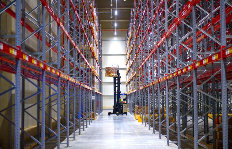 A forklift truck lifts goods into a storage rack in a warehouse of a logistics company.
