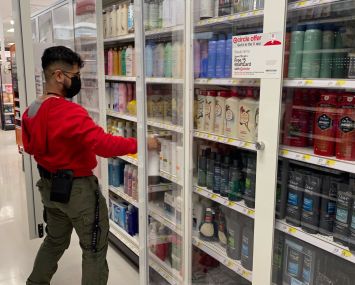 Target employee stocking personal hygiene items in new locked security shelving, Target, Queens, New York.