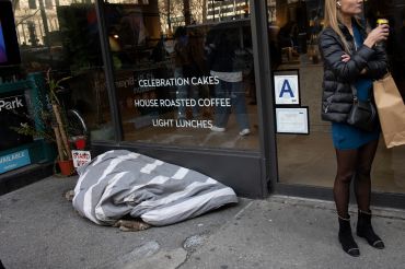 A man sleeps on the street while a woman drinks her coffee this past March in New York City.