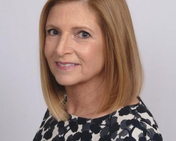 A woman's head turning to the camera and smiling.